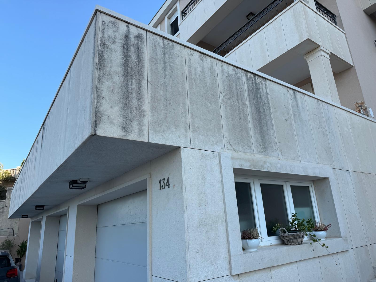 Kamena obloga kuće prije čišćenja, s tamnim tragovima naslaga na balkonskom zidu